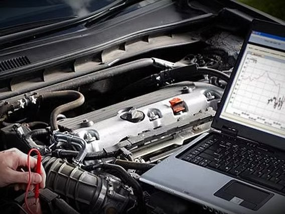 Laptop met meetgrafiek naast een open motorruimte – uitlezen en diagnose van een wagen